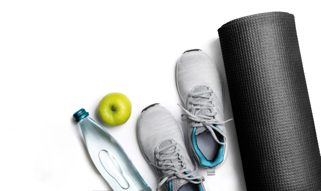 A water bottle, apple, pair of athletic shoes, and rolled up yoga mat.