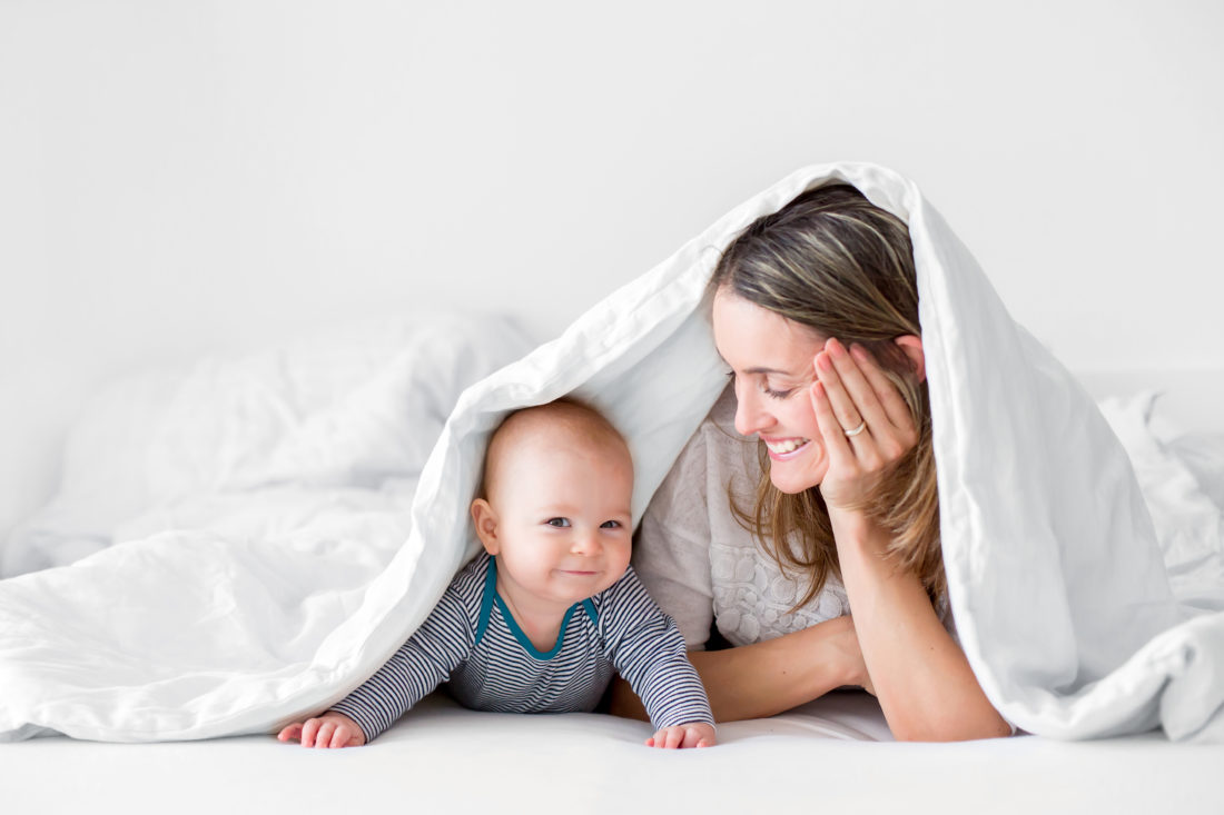 A woman and a baby lie beneath a blanket.