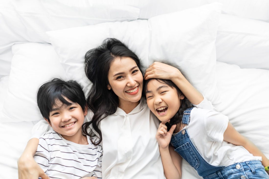 A woman and 2 smiling children lie down together.