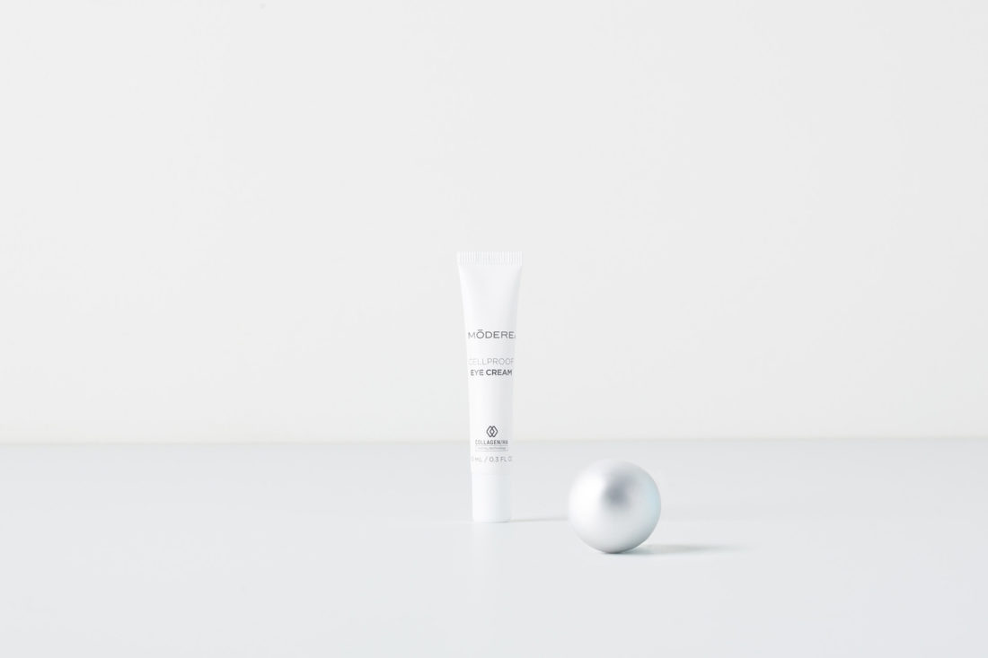 A tube of Modere CellProof Eye Cream. Next to the tube is a small, silver Christmas ornament.