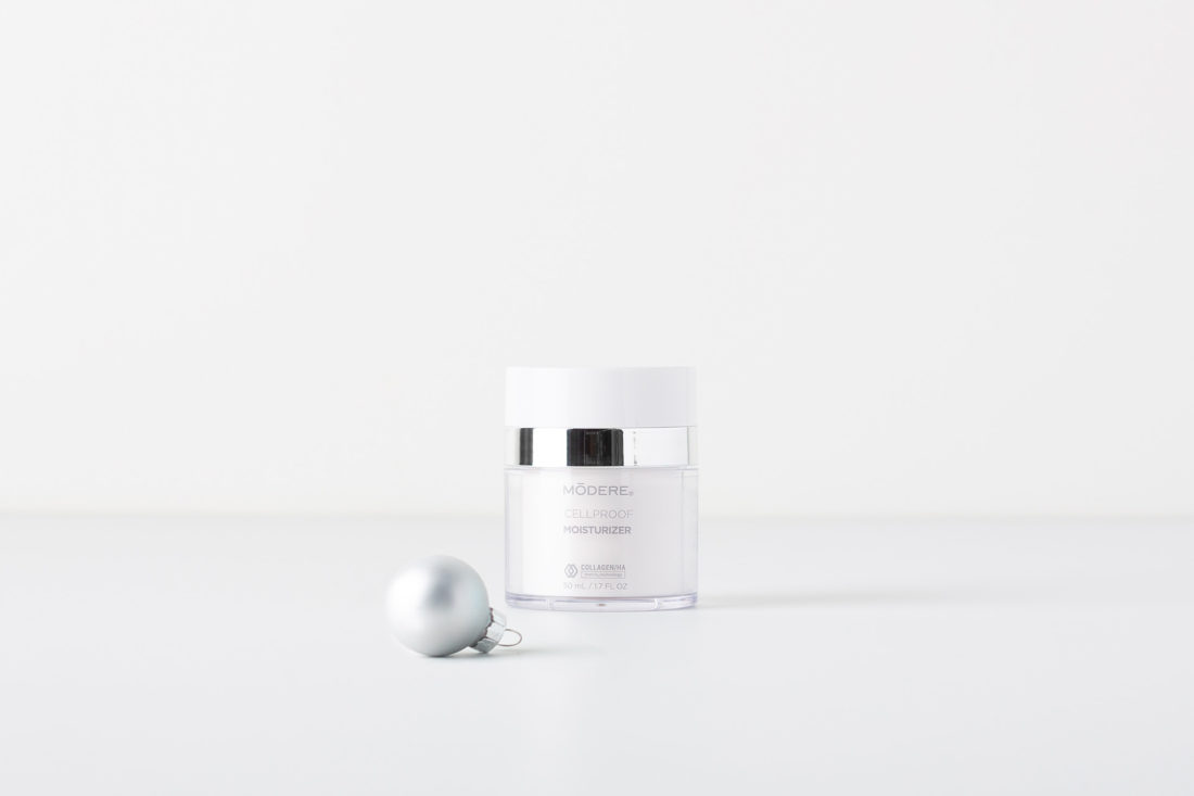 A bottle of Modere CellProof Moisturizer. Next to the bottle is a small, silver Christmas ornament.